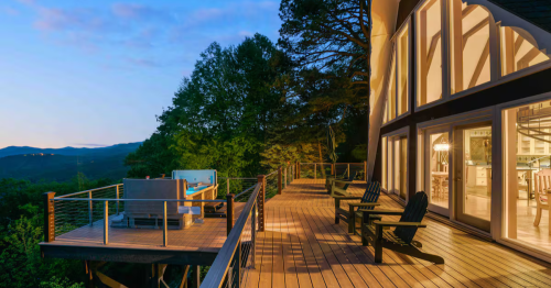 Deck in the back of a chalet Airbnb in North Carolina, with a hot tub and wall of glowing windows