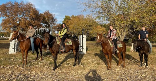 Guests on horseback, holding hands near the farmhouse rental. Scenic rural vacation experience.