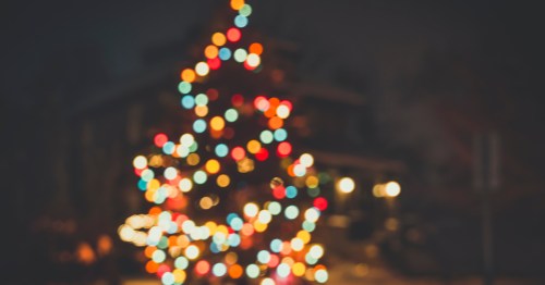A blurred photo of an outdoor Christmas tree with colorful bulbs.