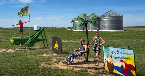 a woman and her daughter sitting under fake palm trees with farm grain bins in the background