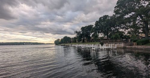 A dock extending out into a lake with trees surrounding the lakefront.