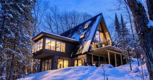 The exterior of an A-frame cabin in a snowy forest.
