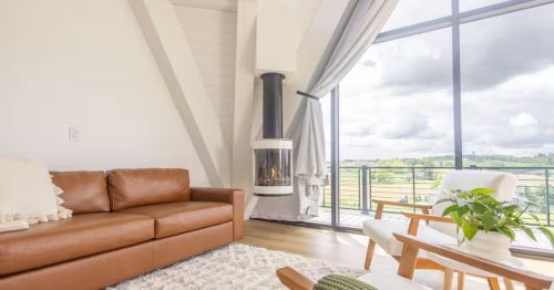The interior white living room of an A-frame with a fire pit and large windows.