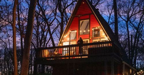 A woman standing on the deck of an A-frame cabin at night.
