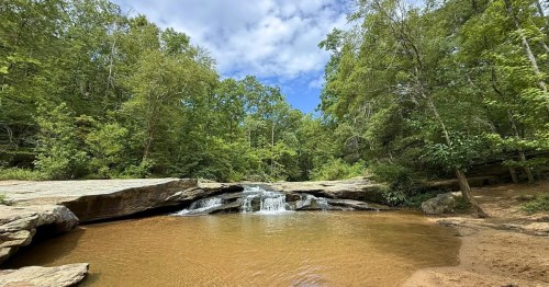 A beautiful cascading waterfall splits down the middle over granite rocks into a light brown pool below.