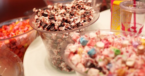 Close-up of clear bowls filled with bulk candy, prominently featuring individually wrapped Tootsie Rolls and assorted taffy.
