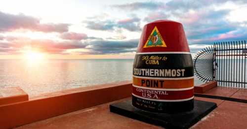 Key West Southernmost Point with a setting sun in the background.
