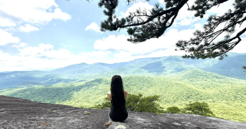 A female hiker sits on a rocky ledge overlooking the Blue Ridge Mountains in North Carolina.