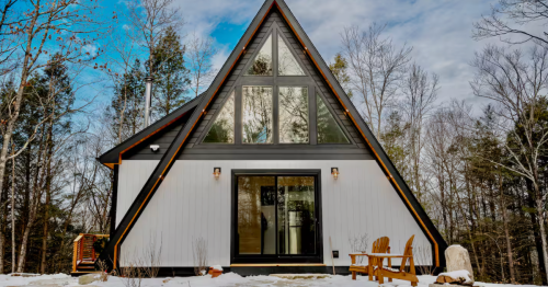 A striking black and white A-frame cabin in a snowy forest, featuring large, geometric windows and a glass front door.