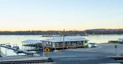 Floating buildings on the river of a waterfront town with golden hour light on the water and bare, winter trees in the background