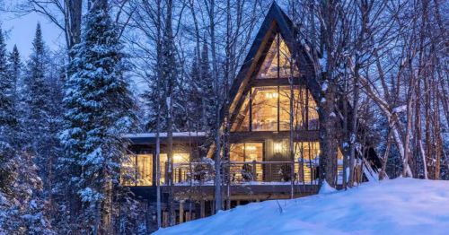 The exterior of an A-frame cabin in a snowy forest.