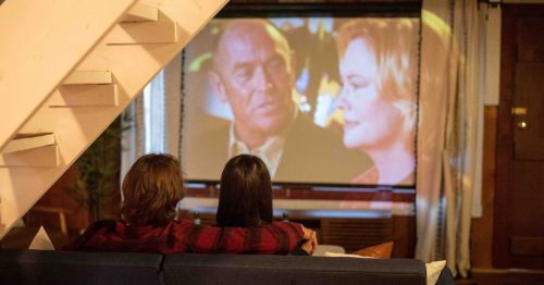 A couple is sitting on a couch watching a movie on a projector.