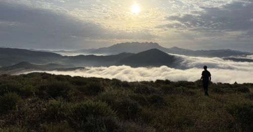 The sun peeks behind clouds that sit above a lush valley. Fog rolls in and begins to cover the vegetation in Southern California.