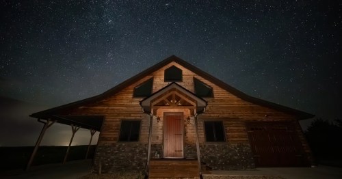 Looking up toward a cabin that is sitting under a blanket of stars.