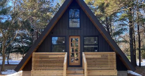 A black A-frame cabin with a wooden deck.