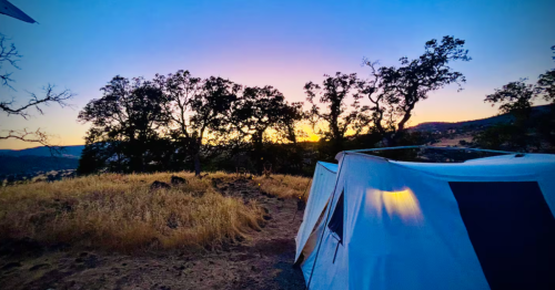 A remote glamping tent at night, while the sunset creates a purple and blue sky above it.