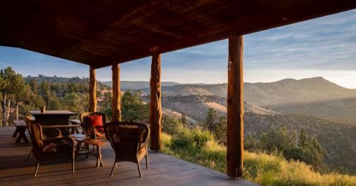 Chairs and a picnic table sit on a covered porch, overlooking hills and a desert-like landscape.