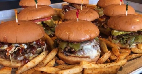 Nine burgers with toothpicks coming out the top sit on a tray filled with French fries.