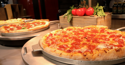 A large pepperoni pizza from Sal's Pizza is set on a table is in the forefront of the picture with two other pizzas in the background.
