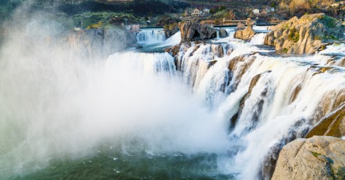 A wide, powerful waterfall tumbles into a river below and spray rises above the water.