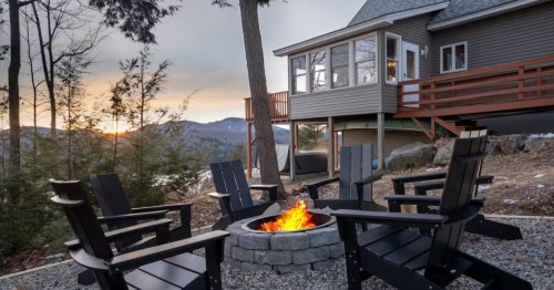 An elevated cabin on a hillside, with a firepit outside at sunset.