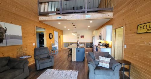 The interior of a home with wooden walls, gray furniture, and a loft.