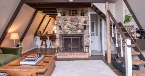 The interior of an A-frame cabin with a fireplace, stairs, and a living room.