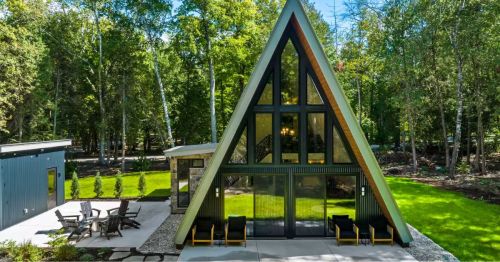 The exterior of a green A-frame cabin with a concrete patio.