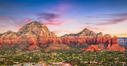 Scenic view of Sedona, Arizona with stunning red rock formations and pastel sunset sky overlooking the town below.