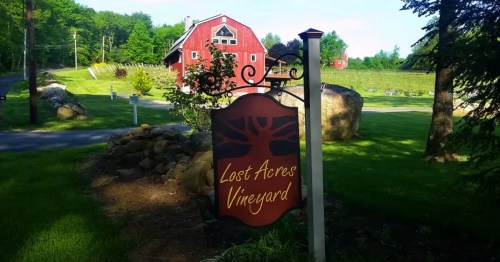 A sign reading "Lost Acres Vineyard" with a red farmhouse in the background.