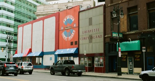 A red and white restaurant building along a busy street with several cars and the words "American Coney Island" on the wall in a circle