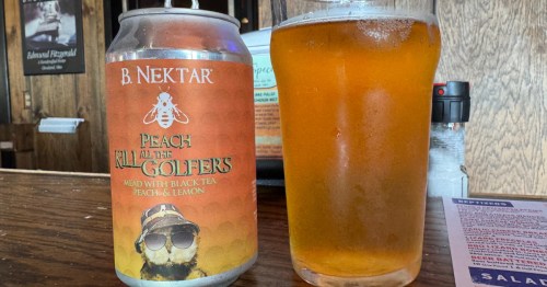 Bright orange mead in a clear glass beside an orange and yellow mead can with a gopher on it. The can says B. Nektar Kill All the Golfers
