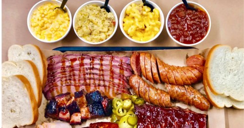 A BBQ platter with sliced brisket, sausage, ribs, burnt ends, bread, pickled peppers, and four sides above.