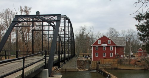 View of a black truss bridge and a historic red mill/barn over a river near Benton, Arkansas.