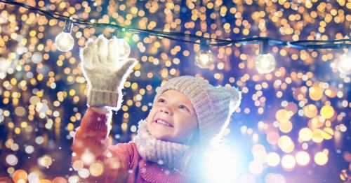 A happy little girl is glaring at sparkling Christmas lights at a festival in a town square.
