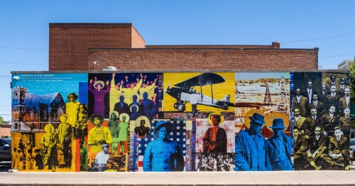 Vibrant outdoor mural depicting historical figures, an airplane, and the city's past.