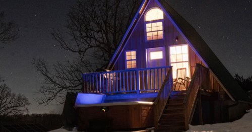exterior of an a-frame Airbnb with a deck and a hot tub aglow with lights at night in compton, arkansas