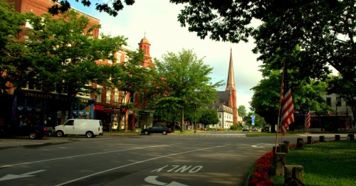 Tree-lined downtown Keene, NH street with historic buildings and a church steeple.
