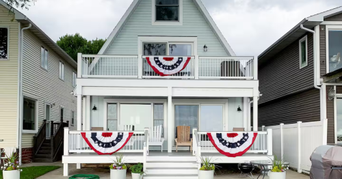 A light blue A-frame house with two decks adorned with red, white, and blue patriotic bunting.