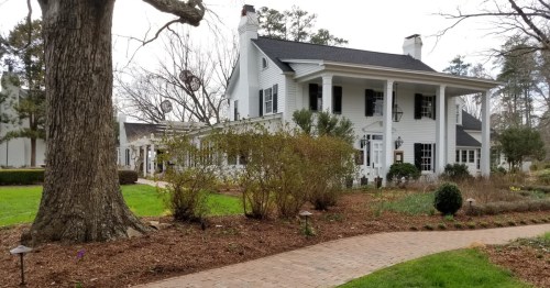 a large white colonial style home with white columns and a beautiful yardin fearrington village nc