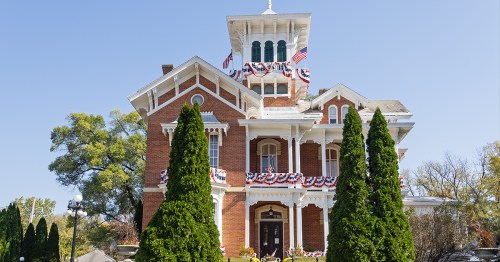 Historic brick home with green trees in front.
