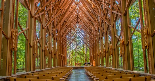 The interior of a wooden and glass church in Arkansas surrounded by a lush forest.