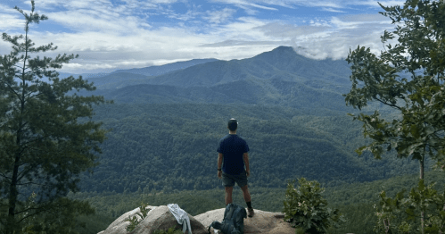 A hiker admires the panoramic mountain view from a Tennessee overlook trail in the summer.