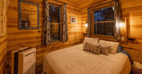 Cabin bedroom with a bed made up with white bedsheets and a pillow that says "love"
