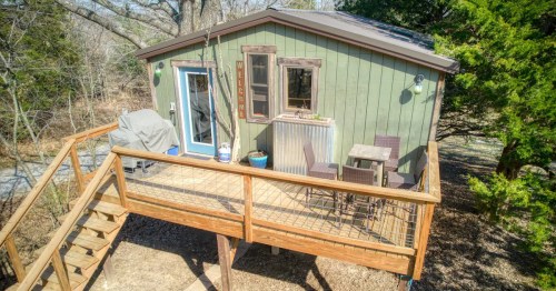 A light green treehouse cabin with a tan wooden stairs and porch in front.