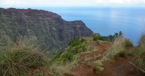 Large sculpted mountains with red dirt and green vegetation tower over the ocean.