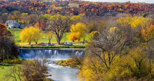 The Root River spills over the Lanesboro dam in picturesque Lanesboro, Minnesota, surrounded by autumn foliage.