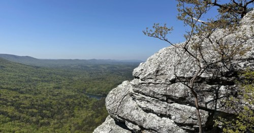 Rocky outcrop gives way to layers of mountains and valley and blue sky overhead
