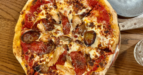 a meat pizza served on a wood board at the bearded barber in anthem arizona