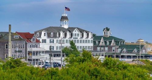 Large buildings in New Shoreham. The main building in the center is a large, white, Victorian style building with an American flag flaying on the roof.
